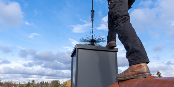 Chimney sweep cleaning a chimney standing on the house roof